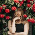 blonde woman standing under rose bush