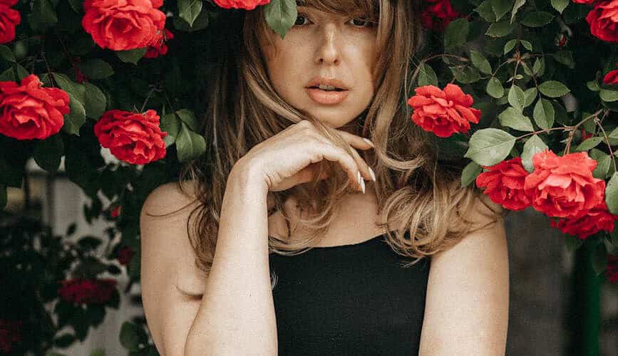 blonde woman standing under rose bush