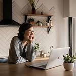 smiling woman talking via laptop in kitchen