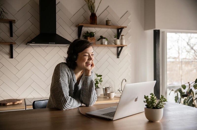 smiling woman talking via laptop in kitchen