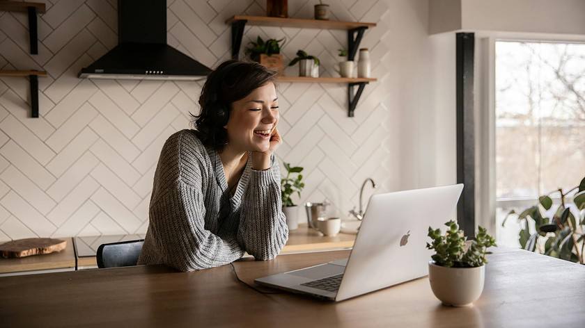 smiling woman talking via laptop in kitchen