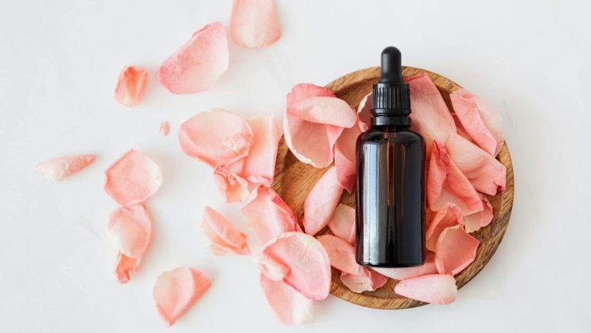 composition of cosmetic bottle with pink rose petals and wooden plate